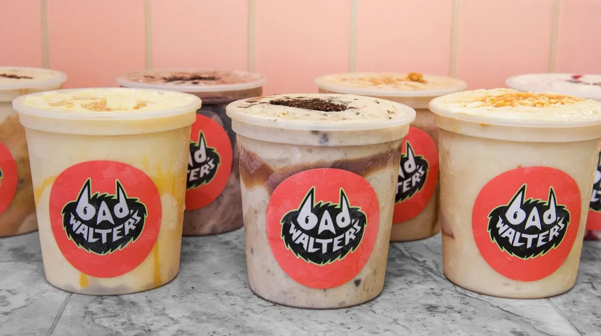 Pints of Bad Walter's ice cream with various toppings, each marked with the shop's red logo sticker, lined up against a pink wall