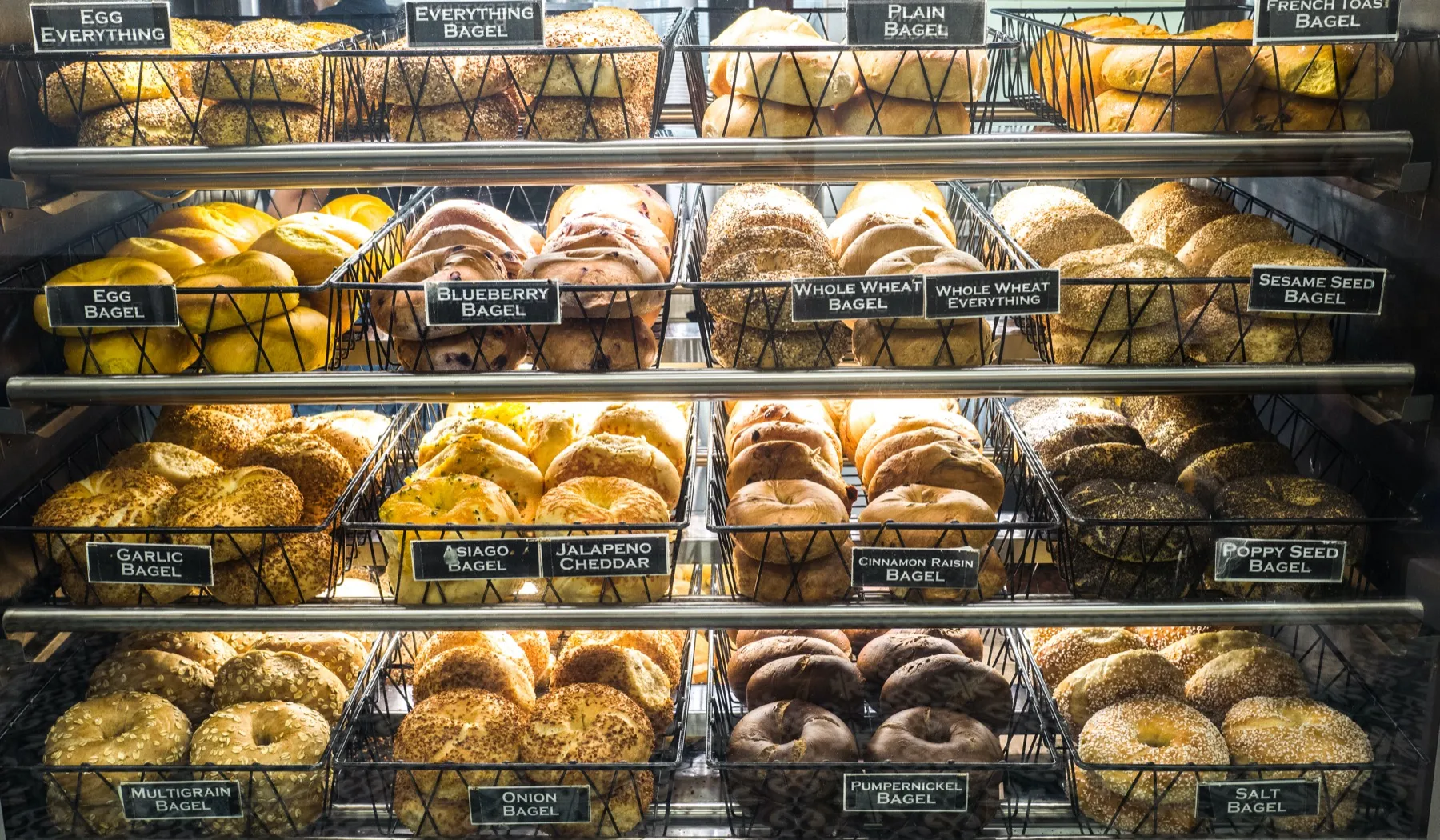 A glass display case filled with baskets of assorted bagels