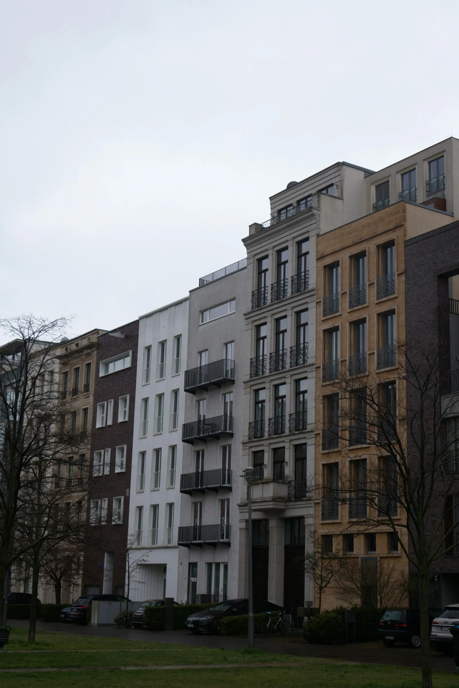 A row of five- to seven-story apartment buildings with distinct narrow facades lining a European street, each built on its own narrow lot
