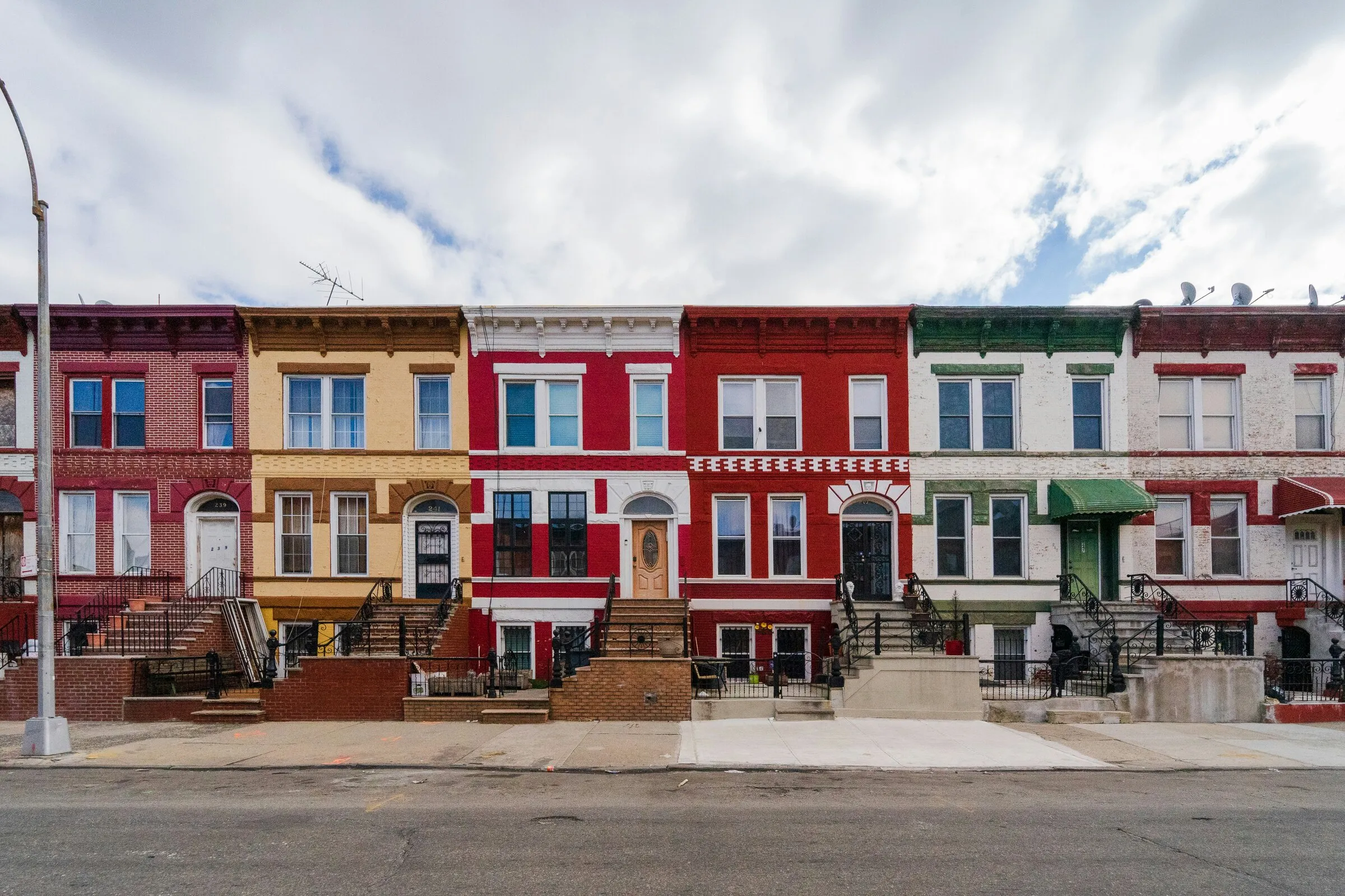 A row of colorful brick rowhouses in red, yellow, and white lining a city street under a cloudy sky