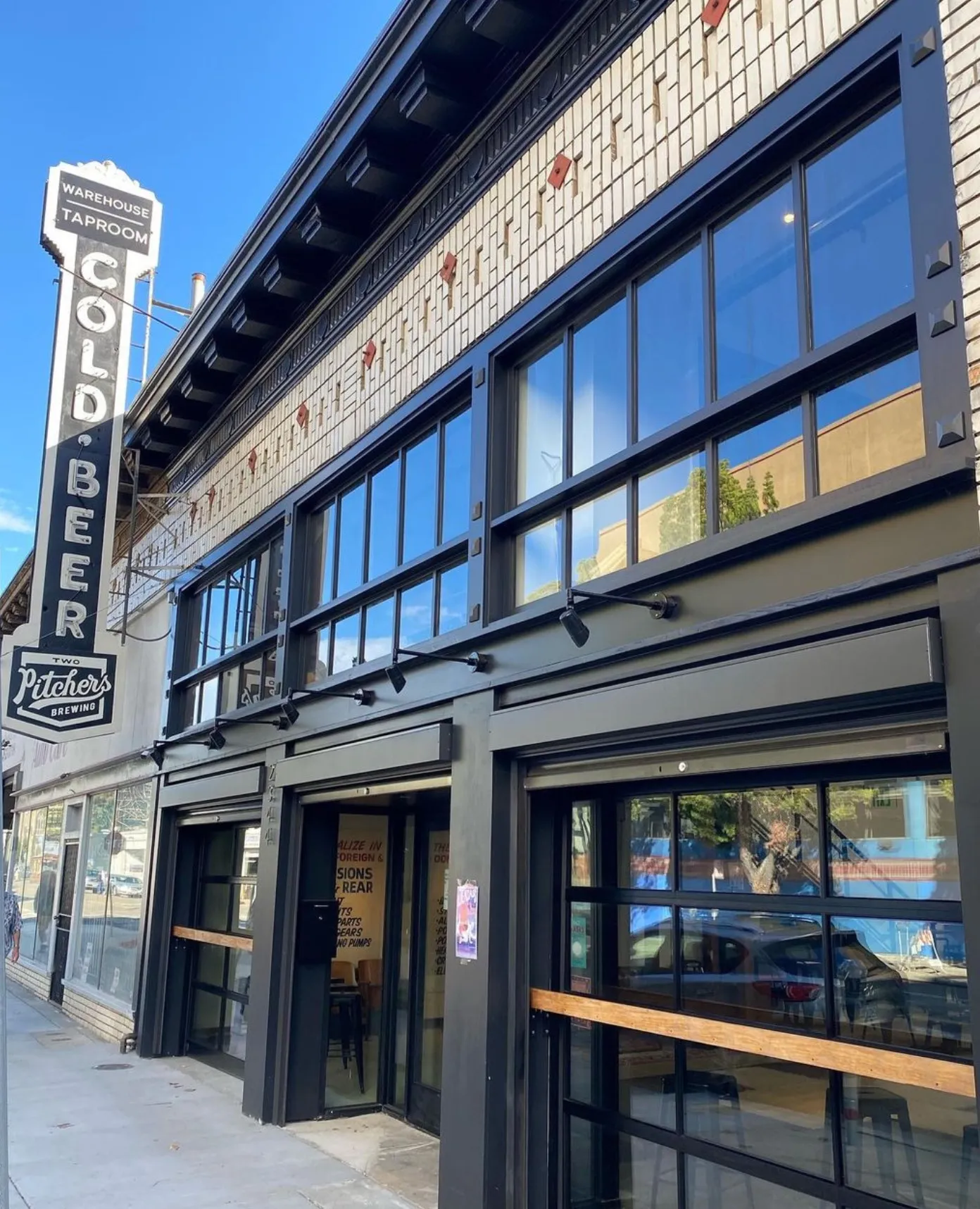 The black storefront of Two Pitchers' Oakland taproom, with large windows and a vertical “Cold Beer” sign